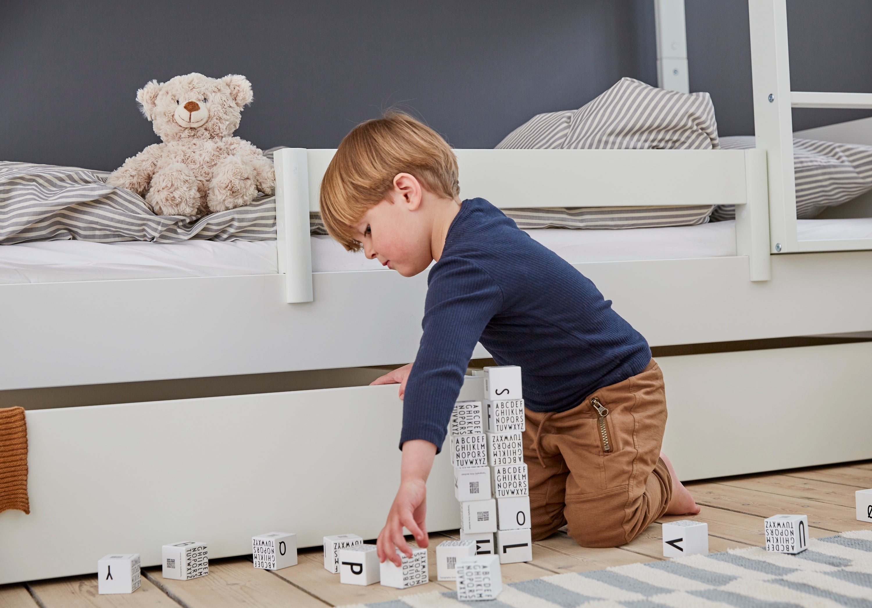Barn leger med bogstavklodser ved Manis-h køjeseng med hvid sengehest.